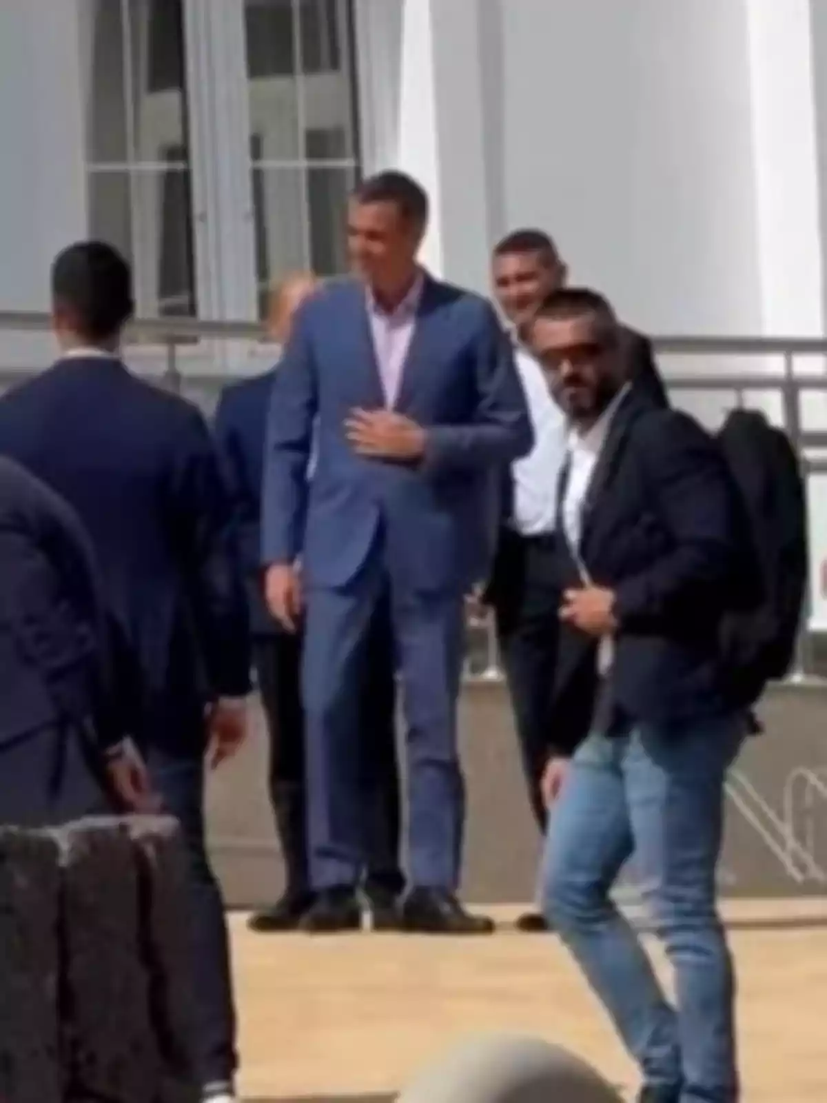 Un grupo de hombres vestidos de traje conversan al aire libre frente a un edificio blanco Un grupo de hombres vestidos de traje conversan al aire libre frente a un edificio blanco
