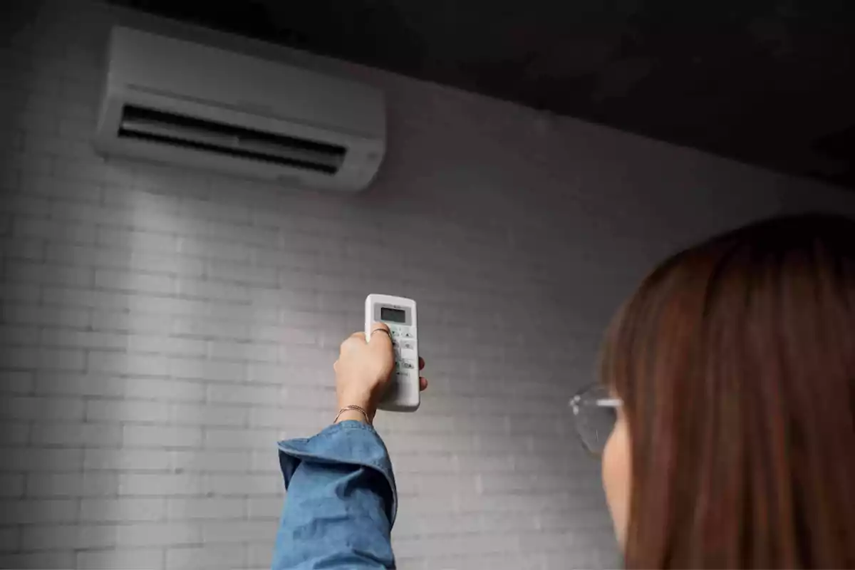 Persona encendiendo un aire acondicionado con un control remoto en una habitación con pared de ladrillos blancos