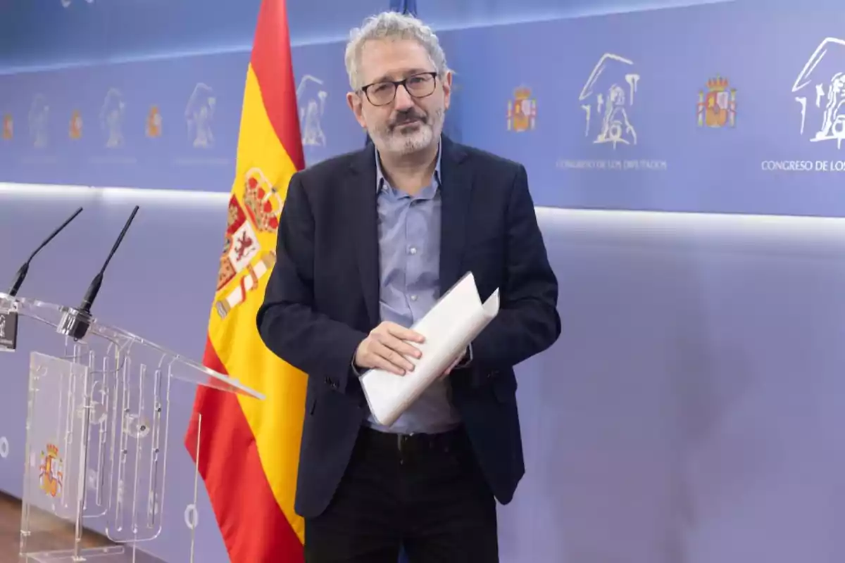 Hombre de cabello canoso y gafas sosteniendo unos papeles frente a un atril con micrófonos y una bandera de España en un fondo institucional del Congreso de los Diputados Hombre de cabello canoso y gafas sosteniendo unos papeles frente a un atril con micrófonos y una bandera de España en un fondo institucional del Congreso de los Diputados