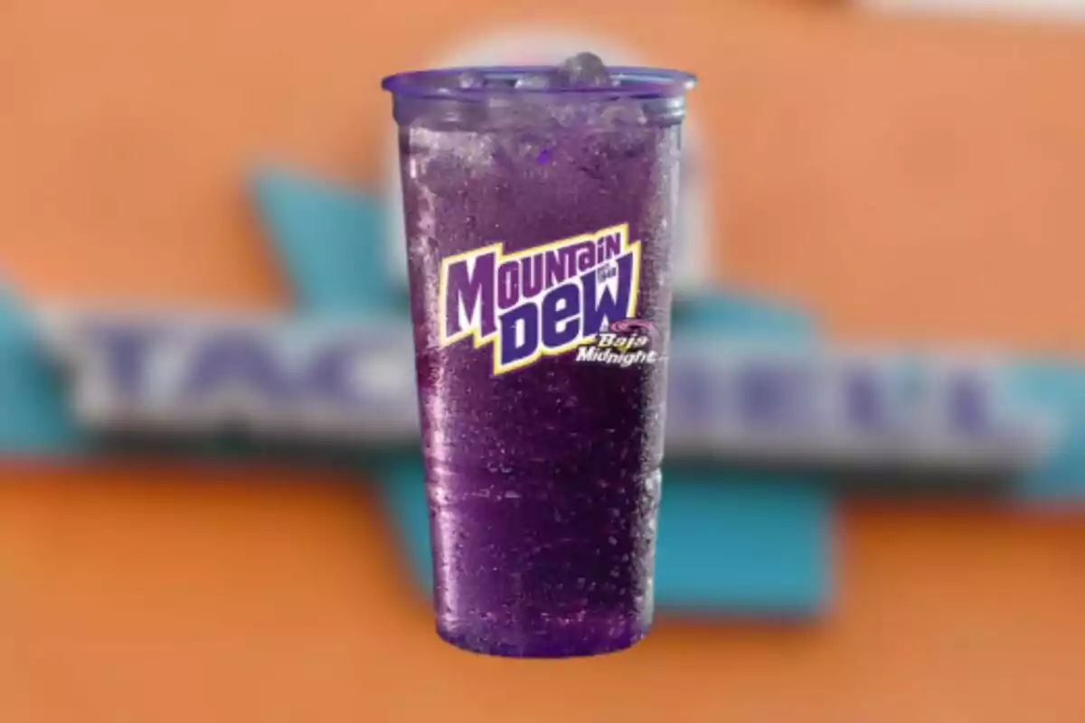 Vaso transparente con bebida morada Mountain Dew Baja Midnight con hielo y fondo desenfocado de colores naranja y azul Vaso transparente con bebida morada Mountain Dew Baja Midnight con hielo y fondo desenfocado de colores naranja y azul