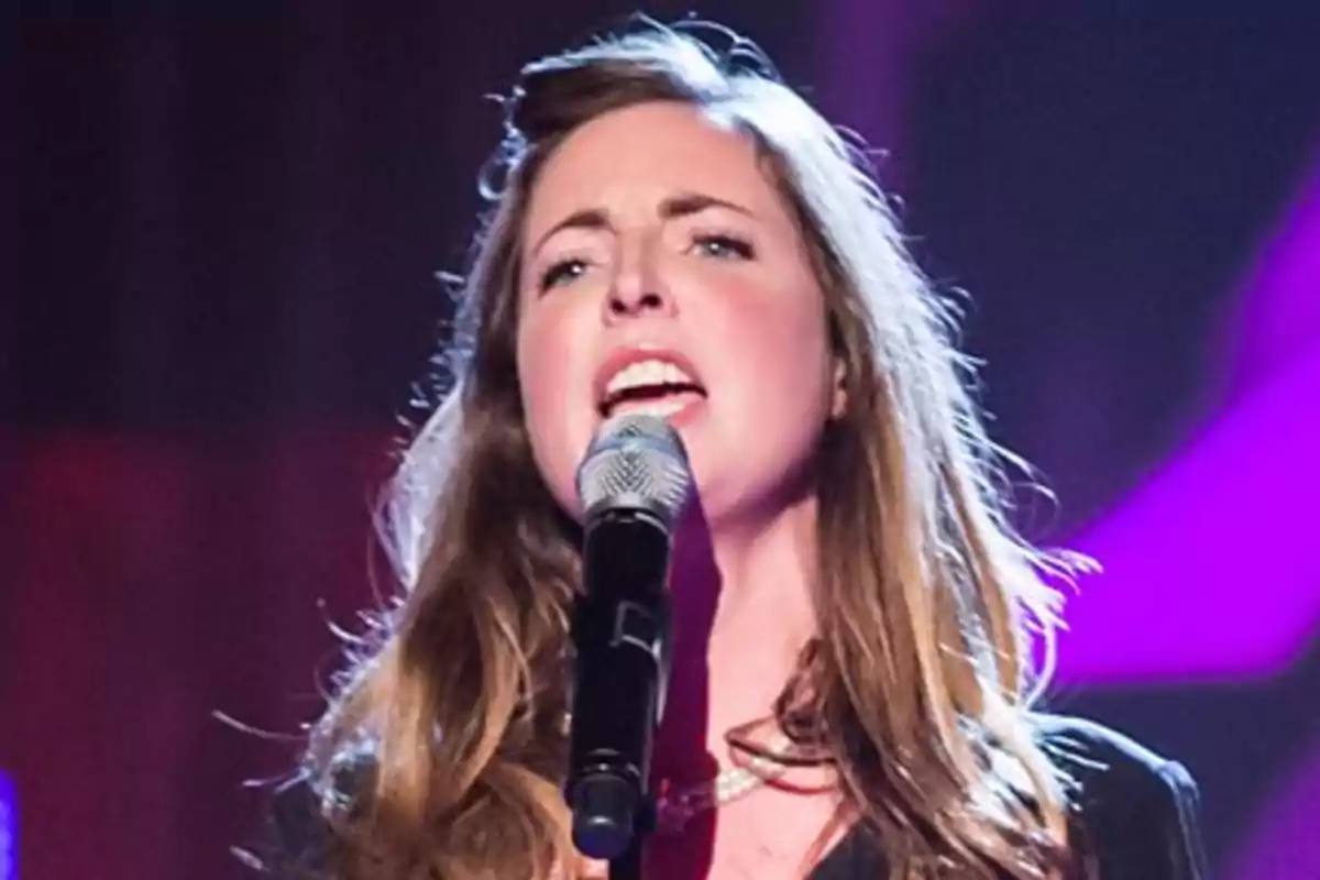Rose Farquhar cantando en un escenario con micrófono en la mano y luces de colores al fondo