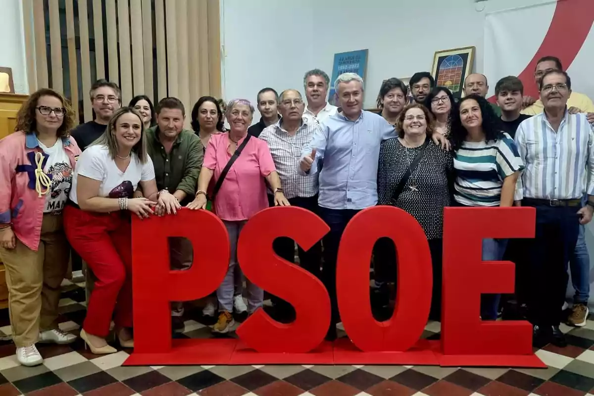 Un grupo de personas sonríe posando detrás de unas grandes letras rojas que forman la palabra PSOE en una sala con suelo de baldosas y cuadros en la pared. Un grupo de personas sonríe posando detrás de unas grandes letras rojas que forman la palabra PSOE en una sala con suelo de baldosas y cuadros en la pared.