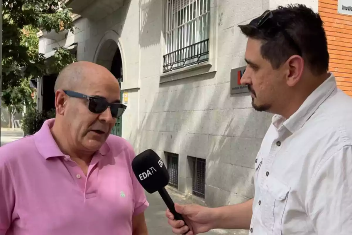 Un hombre con gafas de sol y camiseta rosa es entrevistado en la calle por otra persona que sostiene un micrófono de EDA TV Un hombre con gafas de sol y camiseta rosa es entrevistado en la calle por otra persona que sostiene un micrófono de EDA TV