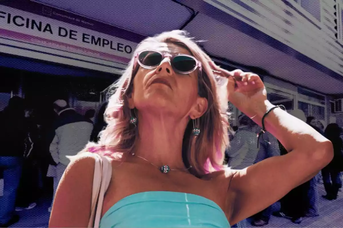 Mujer con gafas de sol y vestido azul claro posando frente a una oficina de empleo con personas haciendo fila al fondo