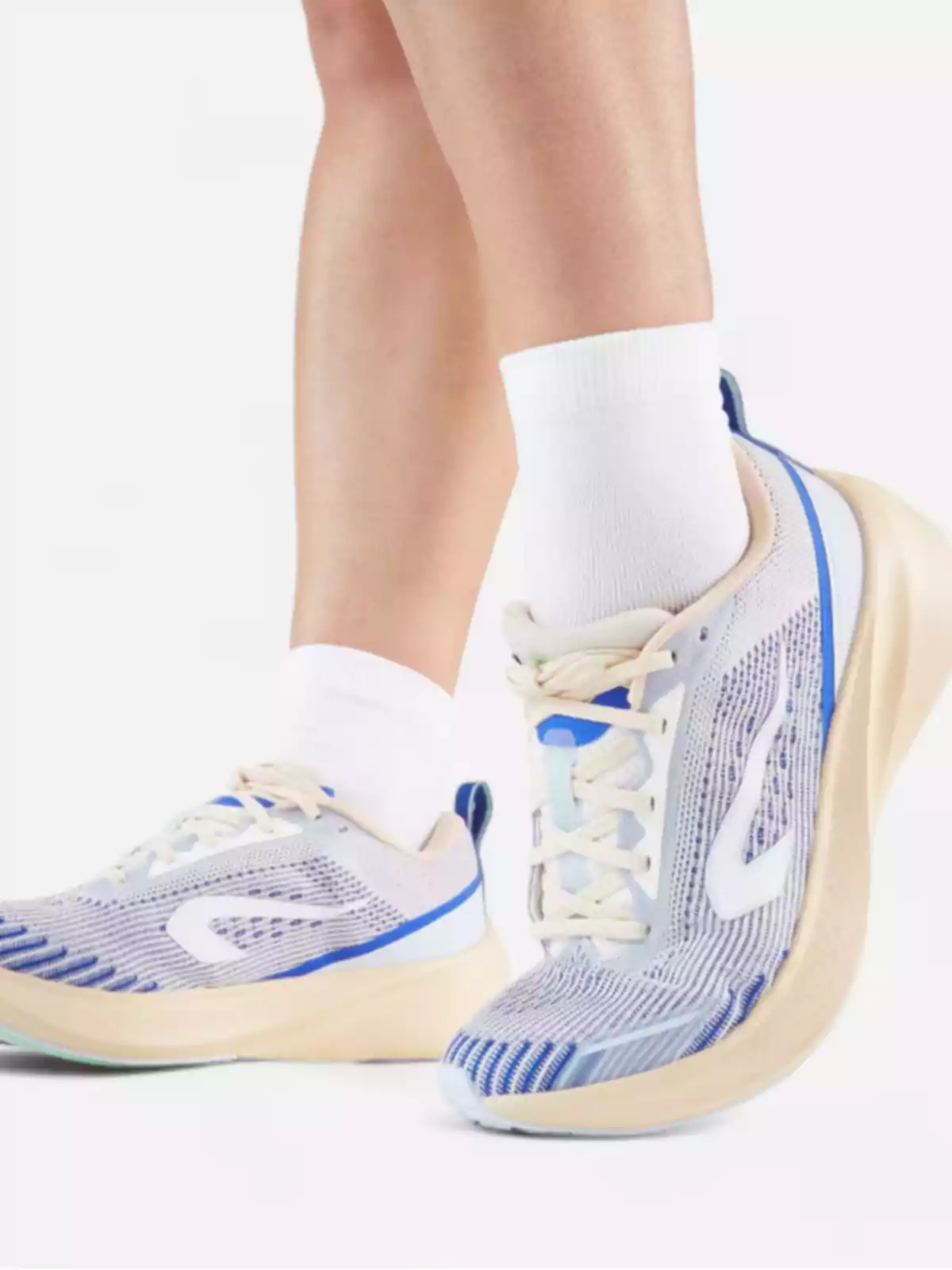 Persona usando calcetas blancas y tenis deportivos en tonos azul, beige y blanco sobre fondo claro Persona usando calcetas blancas y tenis deportivos en tonos azul, beige y blanco sobre fondo claro
