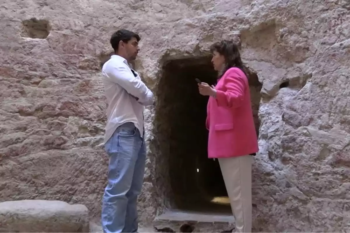 Dos personas conversan frente a una entrada de piedra en lo que parece ser una construcción antigua