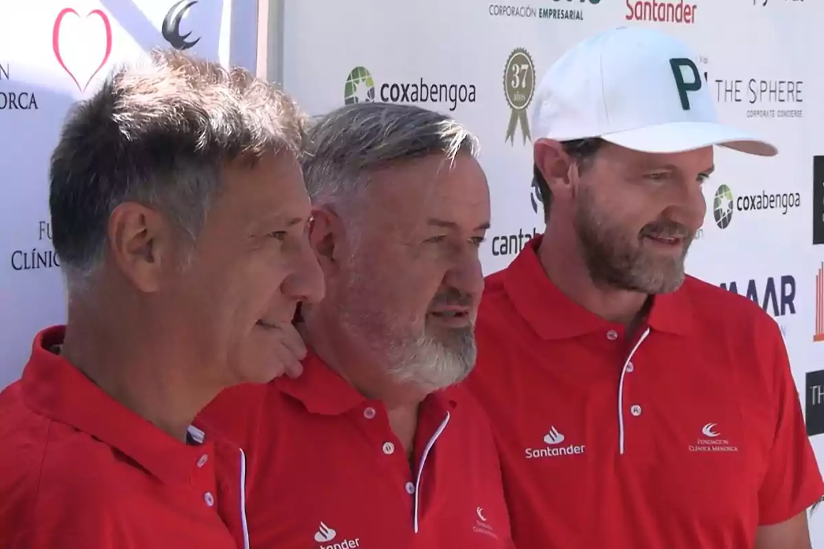 Tres hombres con camisetas rojas y logotipos de Santander posan juntos frente a un fondo con logotipos de patrocinadores Tres hombres con camisetas rojas y logotipos de Santander posan juntos frente a un fondo con logotipos de patrocinadores
