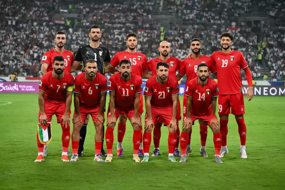 Once jugadores de fútbol con uniforme rojo posan juntos en el campo antes de un partido con un estadio lleno de público al fondo Once jugadores de fútbol con uniforme rojo posan juntos en el campo antes de un partido con un estadio lleno de público al fondo