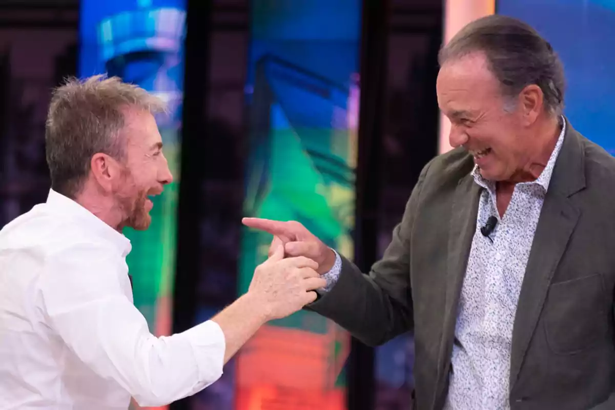 Dos hombres sonríen y se saludan efusivamente en un set de televisión colorido Dos hombres sonríen y se saludan efusivamente en un set de televisión colorido