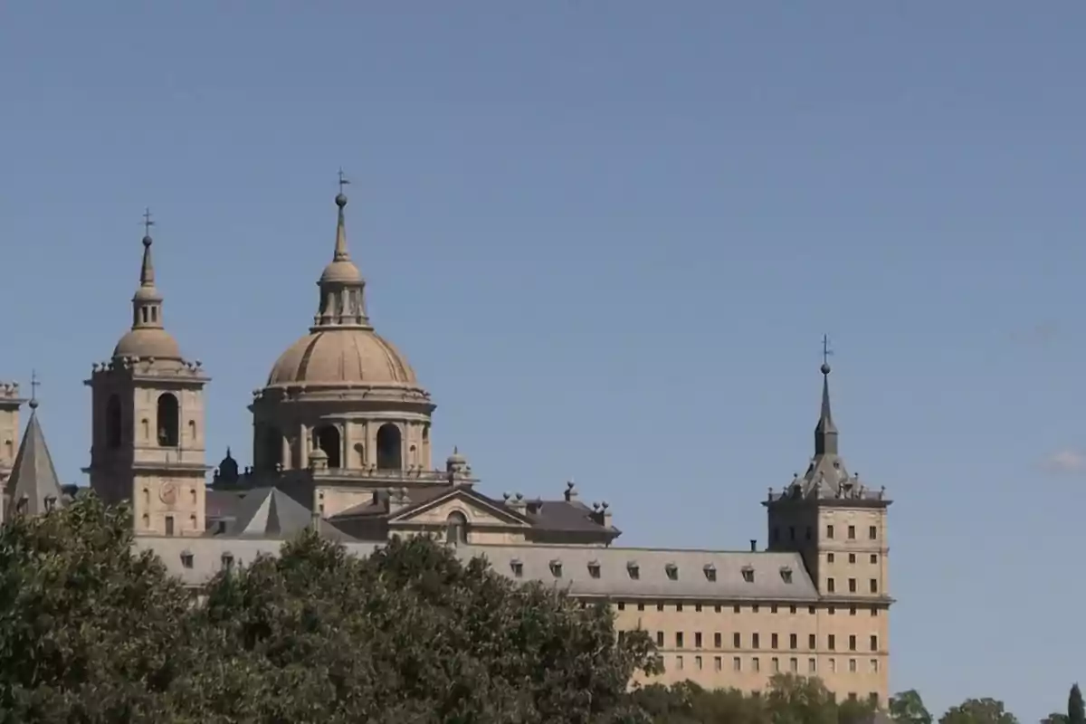Vista del Monasterio de El Escorial con cielo despejado y árboles en primer plano Vista del Monasterio de El Escorial con cielo despejado y árboles en primer plano