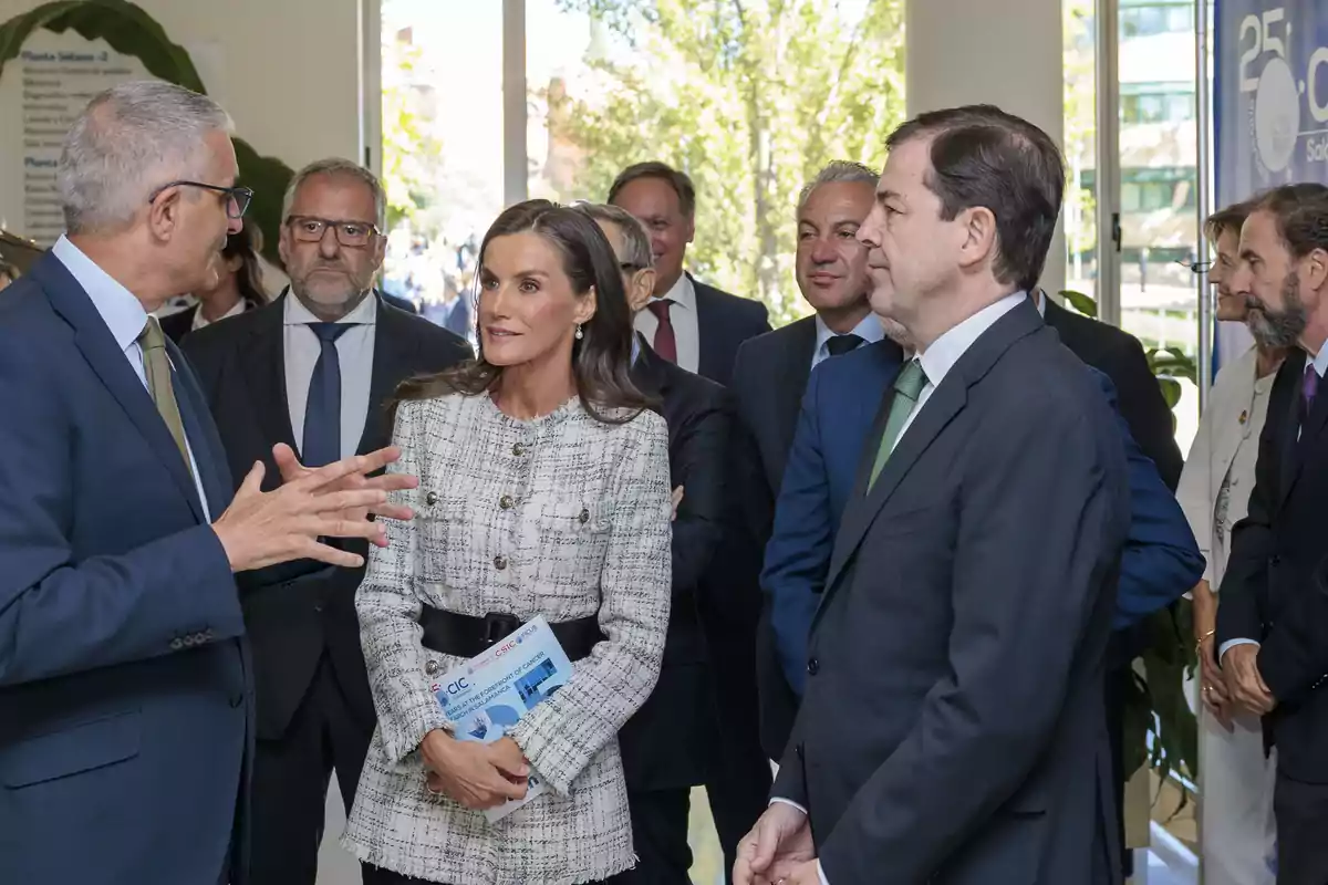 Un grupo de personas vestidas de manera formal conversa en el interior de un edificio iluminado por luz natural que entra por grandes ventanas Un grupo de personas vestidas de manera formal conversa en el interior de un edificio iluminado por luz natural que entra por grandes ventanas