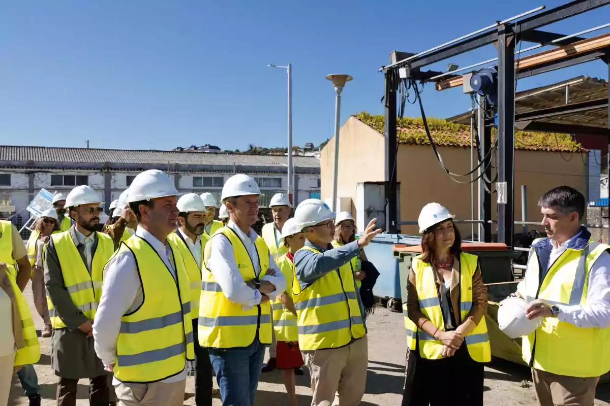 Un grupo de personas con chalecos reflectantes y cascos de seguridad observa una explicación en una obra al aire libre bajo un cielo despejado.