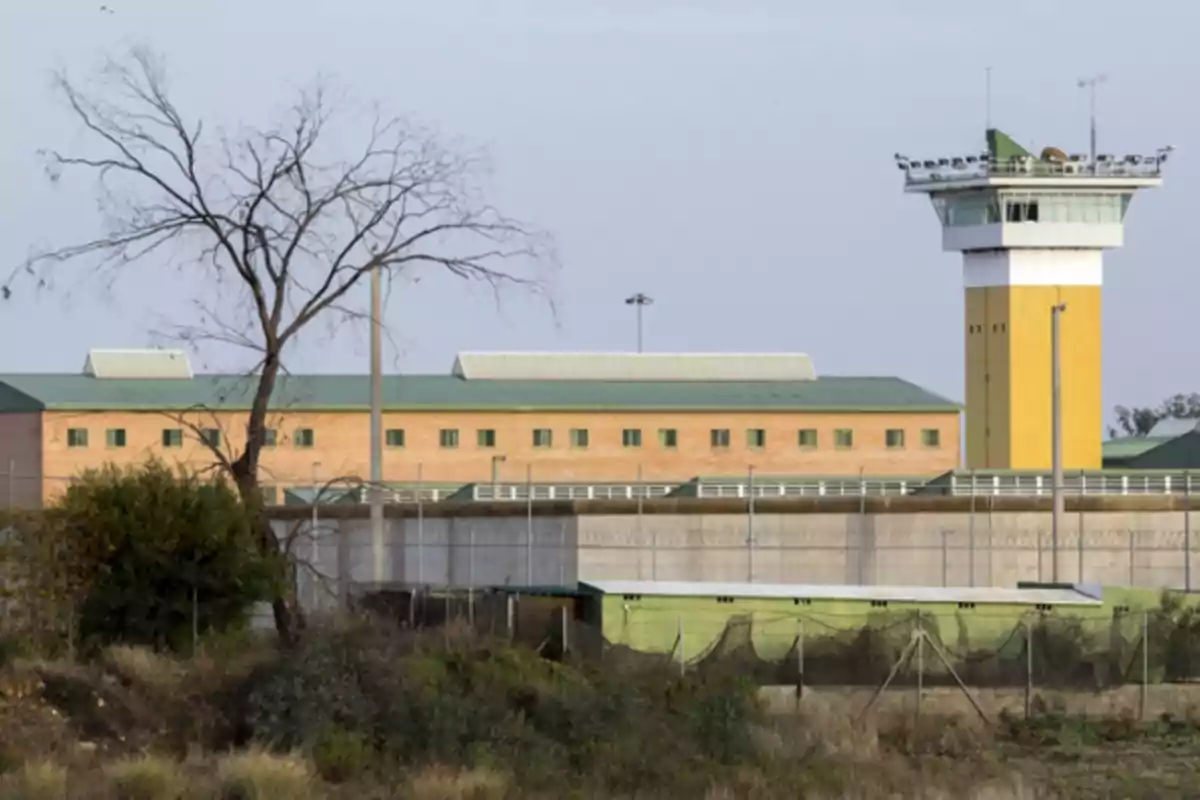 Edificio de una prisión con una torre de vigilancia y un árbol seco en primer plano Edificio de una prisión con una torre de vigilancia y un árbol seco en primer plano