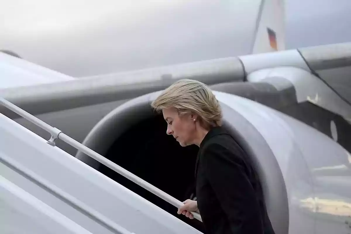 Mujer rubia con saco negro subiendo las escaleras de un avión blanco Mujer rubia con saco negro subiendo las escaleras de un avión blanco