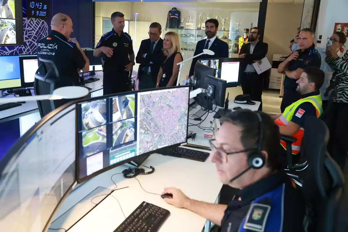 Varios agentes de policía y personal de emergencias trabajan y conversan en una sala de control equipada con múltiples monitores y pantallas de vigilancia. Varios agentes de policía y personal de emergencias trabajan y conversan en una sala de control equipada con múltiples monitores y pantallas de vigilancia.