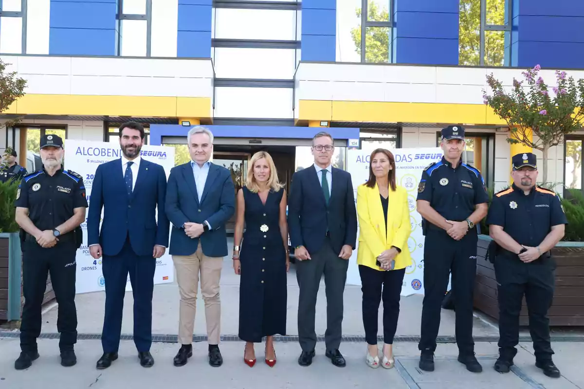 Ocho personas posan frente a un edificio moderno, algunas con uniforme policial y otras con ropa formal, en un evento institucional.