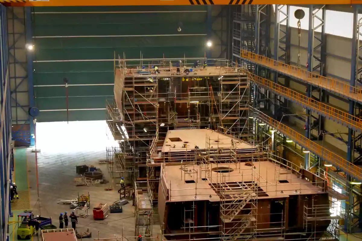 Construcción de un barco en un astillero con andamios y trabajadores alrededor de la estructura