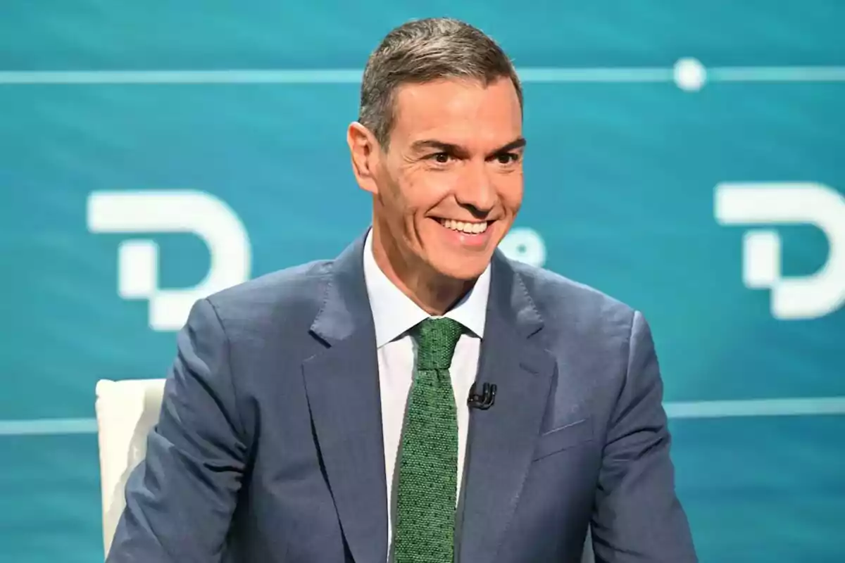 Hombre de cabello corto y canoso con traje azul y corbata verde sonriendo en un entorno de estudio con fondo azul
