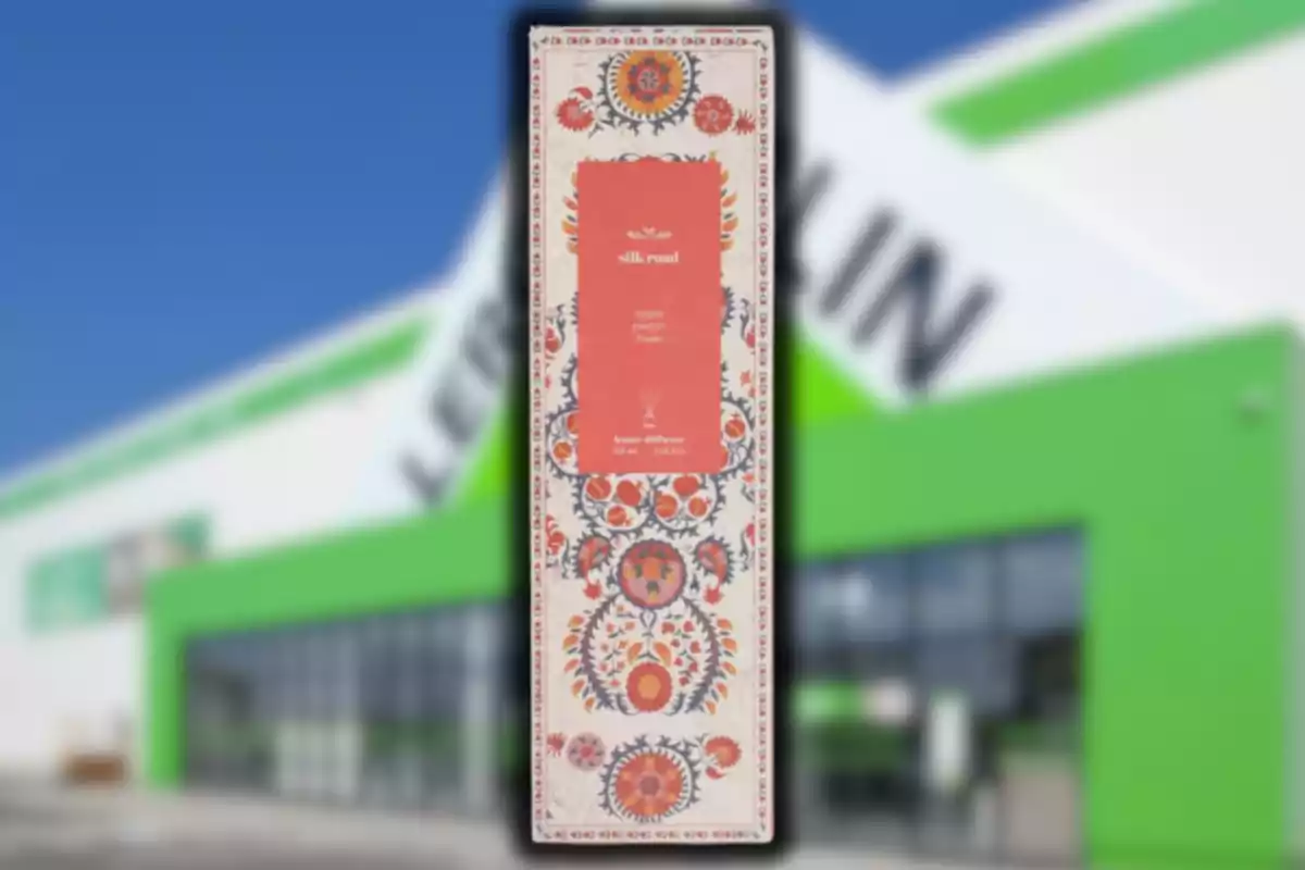 Caja de difusor aromático con diseño floral en primer plano y una tienda con fachada verde y blanca desenfocada al fondo Caja de difusor aromático con diseño floral en primer plano y una tienda con fachada verde y blanca desenfocada al fondo