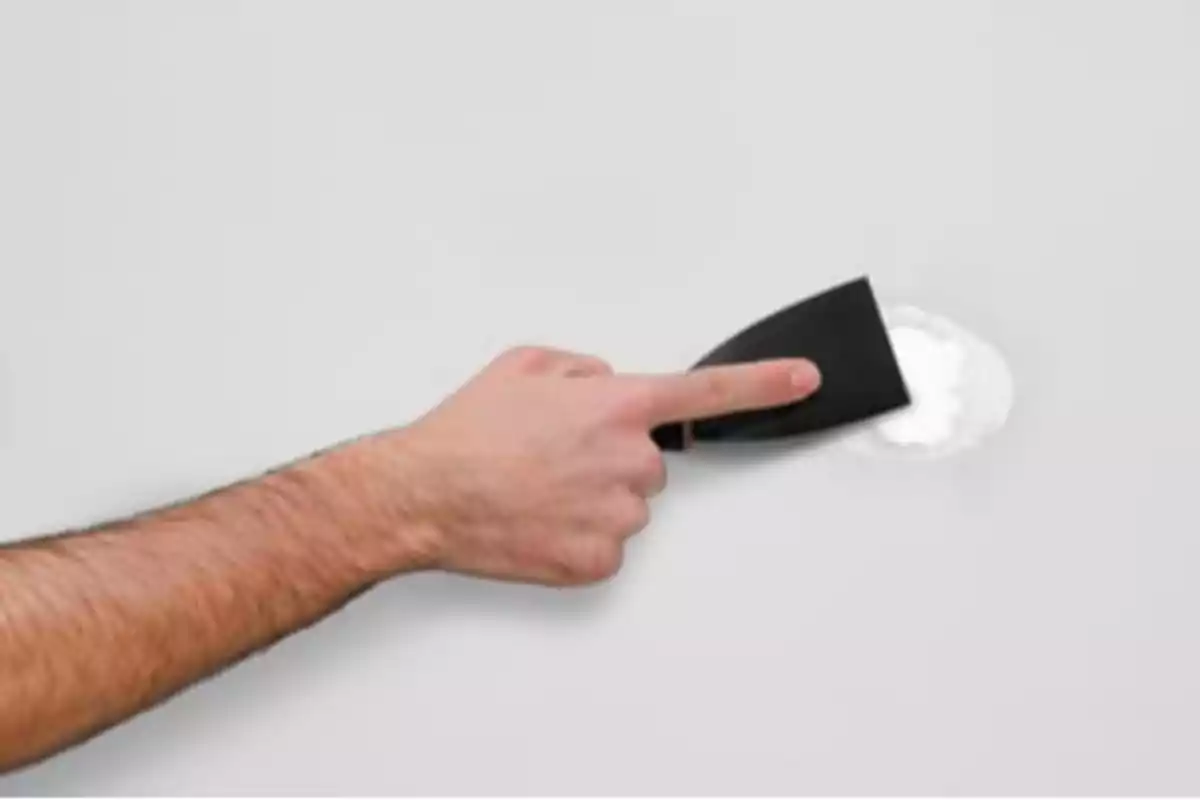 Persona usando una espátula para aplicar masilla en una pared blanca Persona usando una espátula para aplicar masilla en una pared blanca