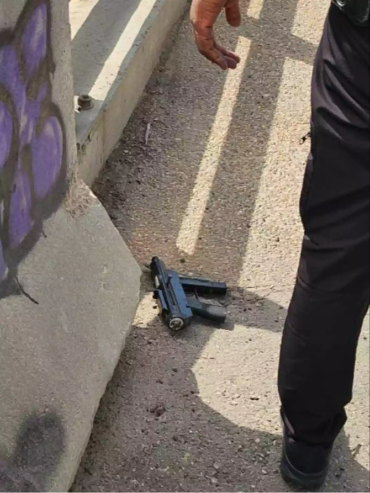 Pistola en el suelo junto a una persona vestida de negro y una pared con graffiti Pistola en el suelo junto a una persona vestida de negro y una pared con graffiti