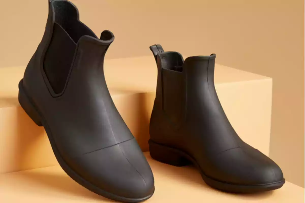 Botines negros de goma con diseño minimalista sobre una superficie beige
