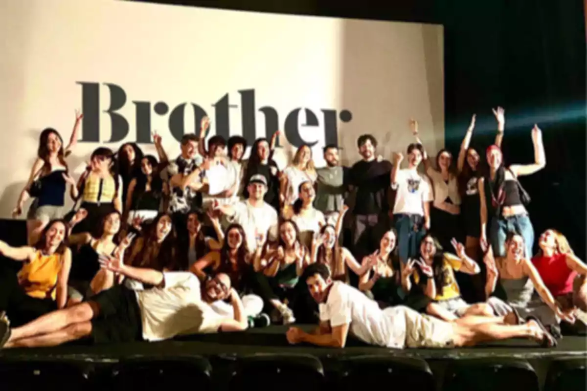 Grupo numeroso de personas posando sonrientes y haciendo gestos de celebración frente a una pantalla grande con la palabra Brother