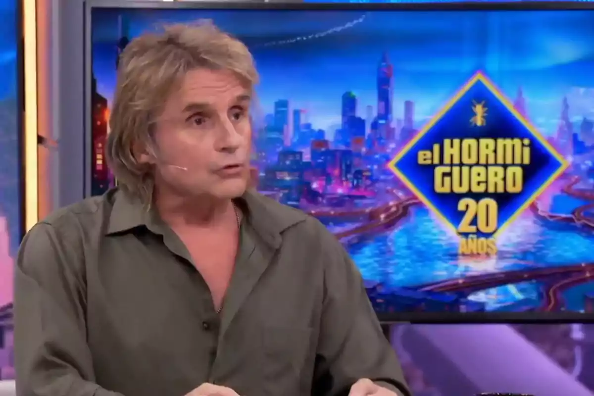 Hombre de cabello rubio y camisa verde hablando en un programa de televisión con el logo de El Hormiguero 20 años al fondo