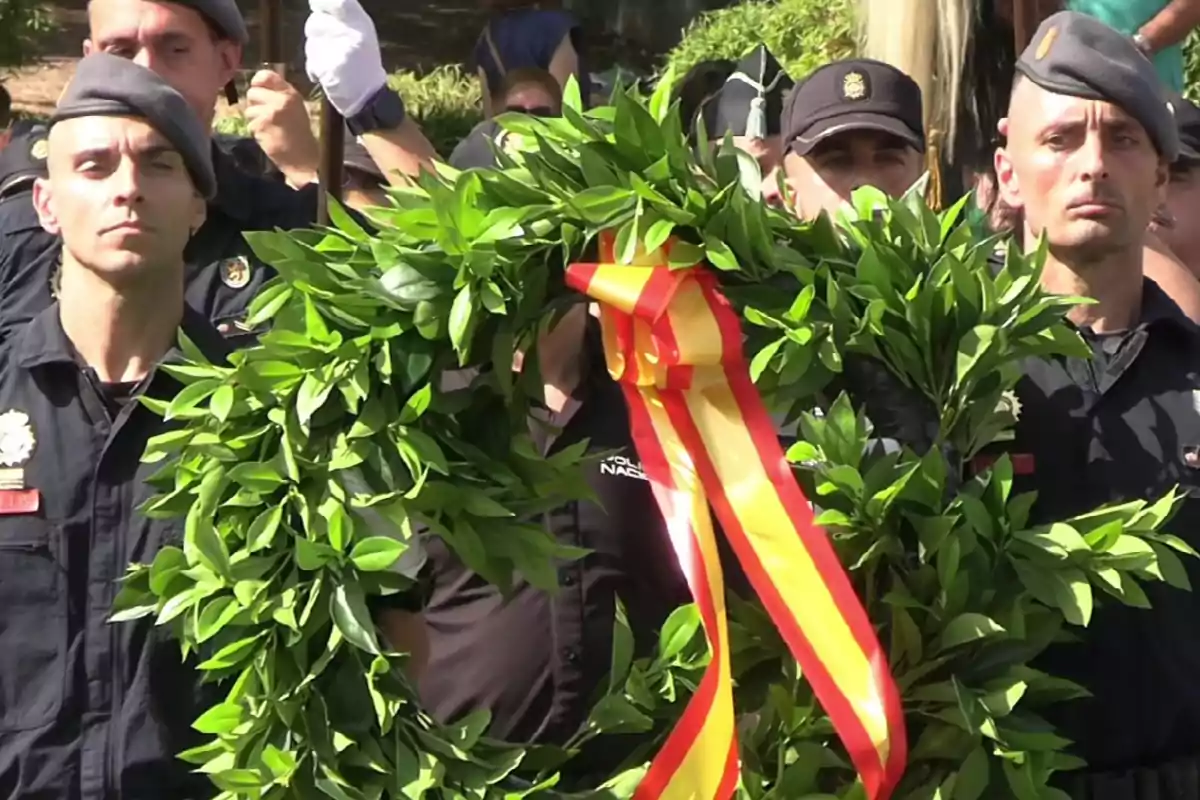 Policías uniformados sostienen una corona de laurel decorada con una cinta de los colores de la bandera de España durante una ceremonia solemne al aire libre Policías uniformados sostienen una corona de laurel decorada con una cinta de los colores de la bandera de España durante una ceremonia solemne al aire libre