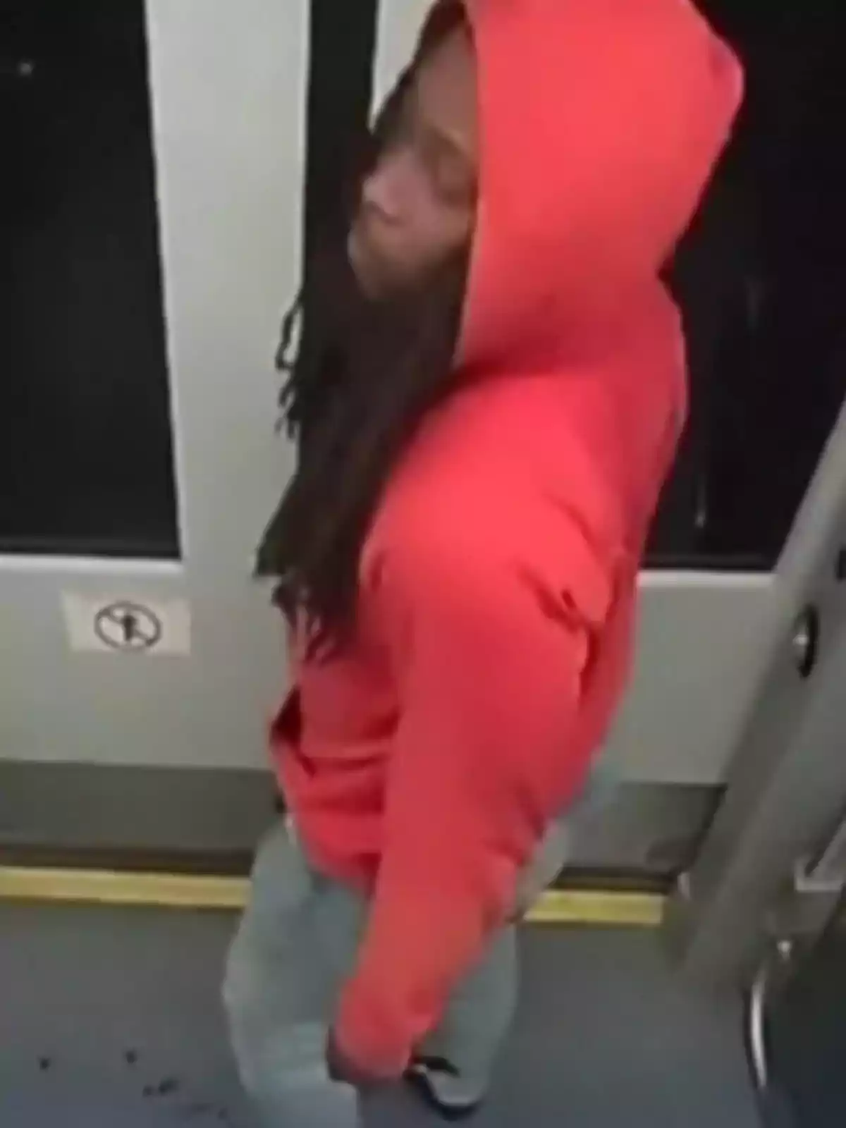 Persona con sudadera roja y capucha puesta de pie dentro de un transporte público