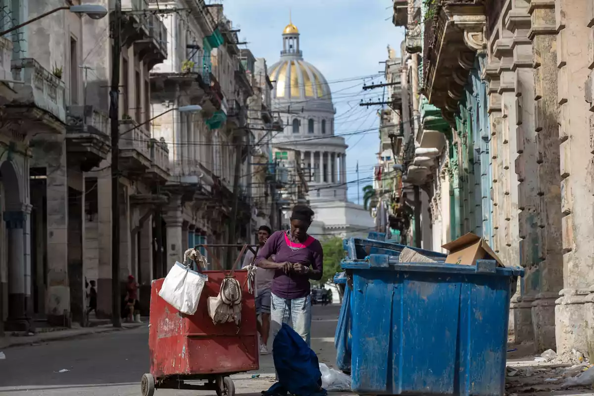 Mujer revisando basura en una calle de La Habana con el Capitolio al fondo y edificios antiguos a los lados Mujer revisando basura en una calle de La Habana con el Capitolio al fondo y edificios antiguos a los lados
