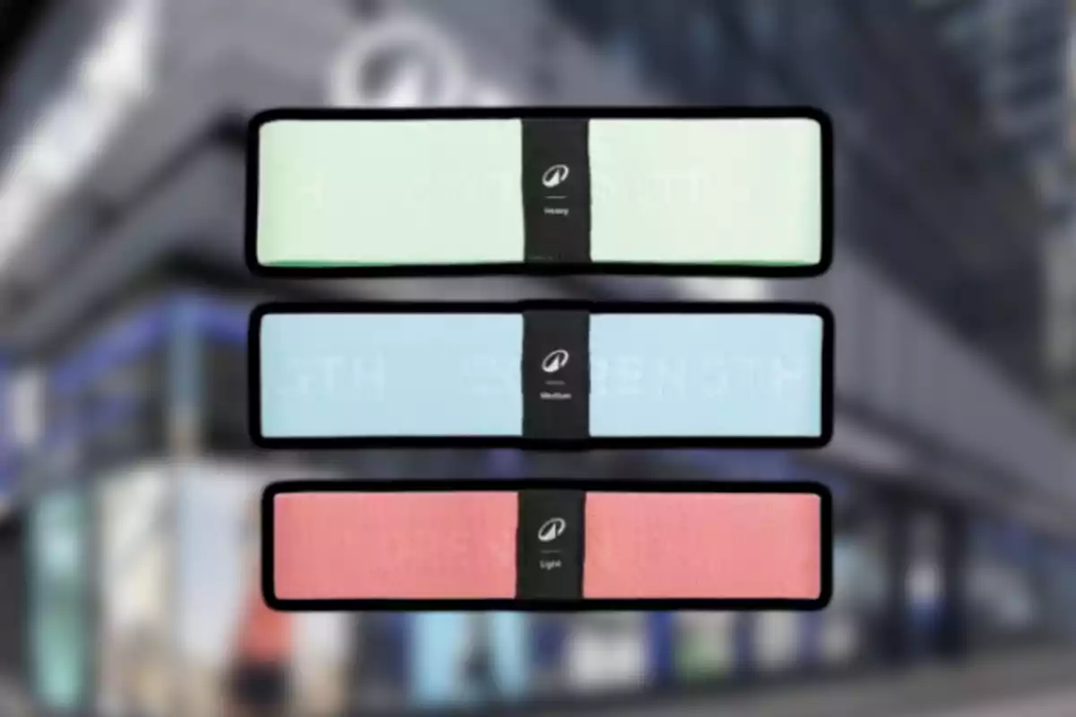Tres bandas elásticas de resistencia en colores verde, azul y rosa con etiquetas negras al centro sobre un fondo desenfocado de edificio. Tres bandas elásticas de resistencia en colores verde, azul y rosa con etiquetas negras al centro sobre un fondo desenfocado de edificio.