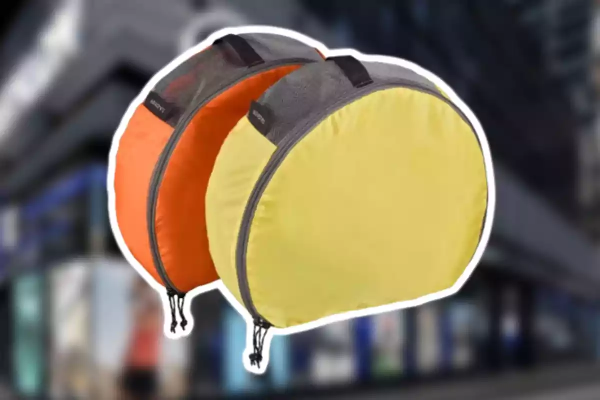 Dos bolsas redondas de tela, una amarilla y una naranja, con cierre y detalles en gris, sobre un fondo desenfocado.