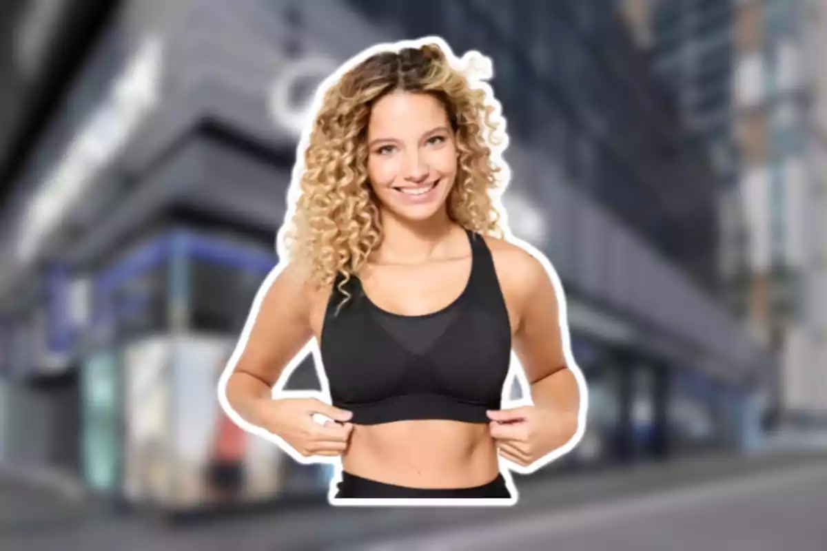Mujer joven de cabello rizado y rubio sonriendo mientras usa ropa deportiva negra con fondo urbano desenfocado