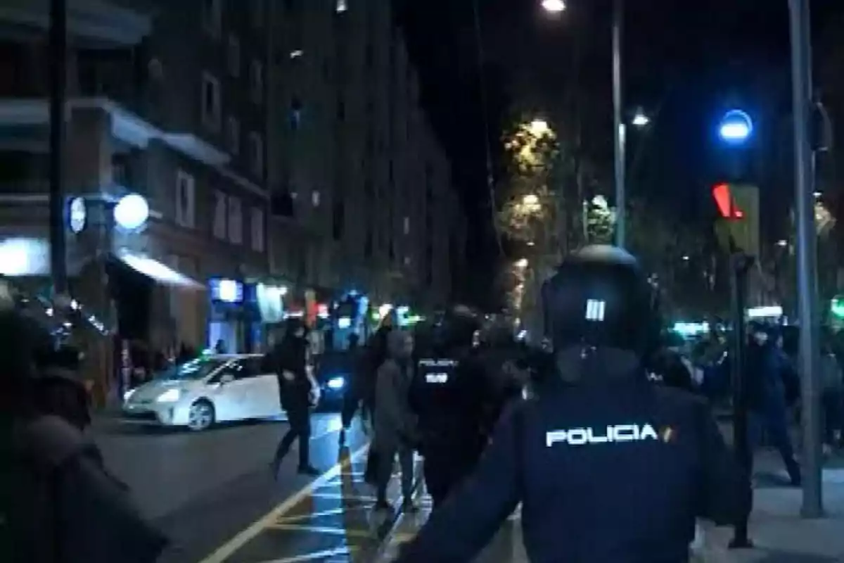 Policías antidisturbios en una calle de noche con luces de la ciudad y personas alrededor