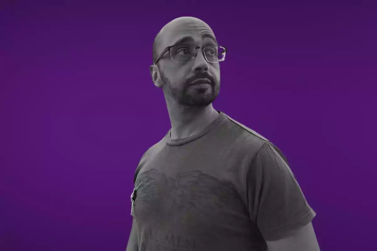 Hombre con gafas y barba mirando hacia un lado sobre un fondo morado