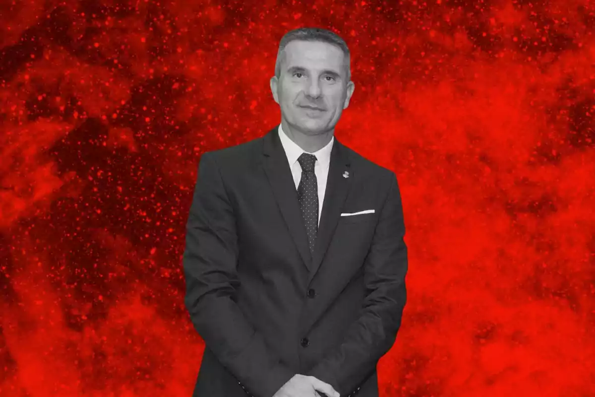 Hombre de traje oscuro posando frente a un fondo rojo con textura abstracta