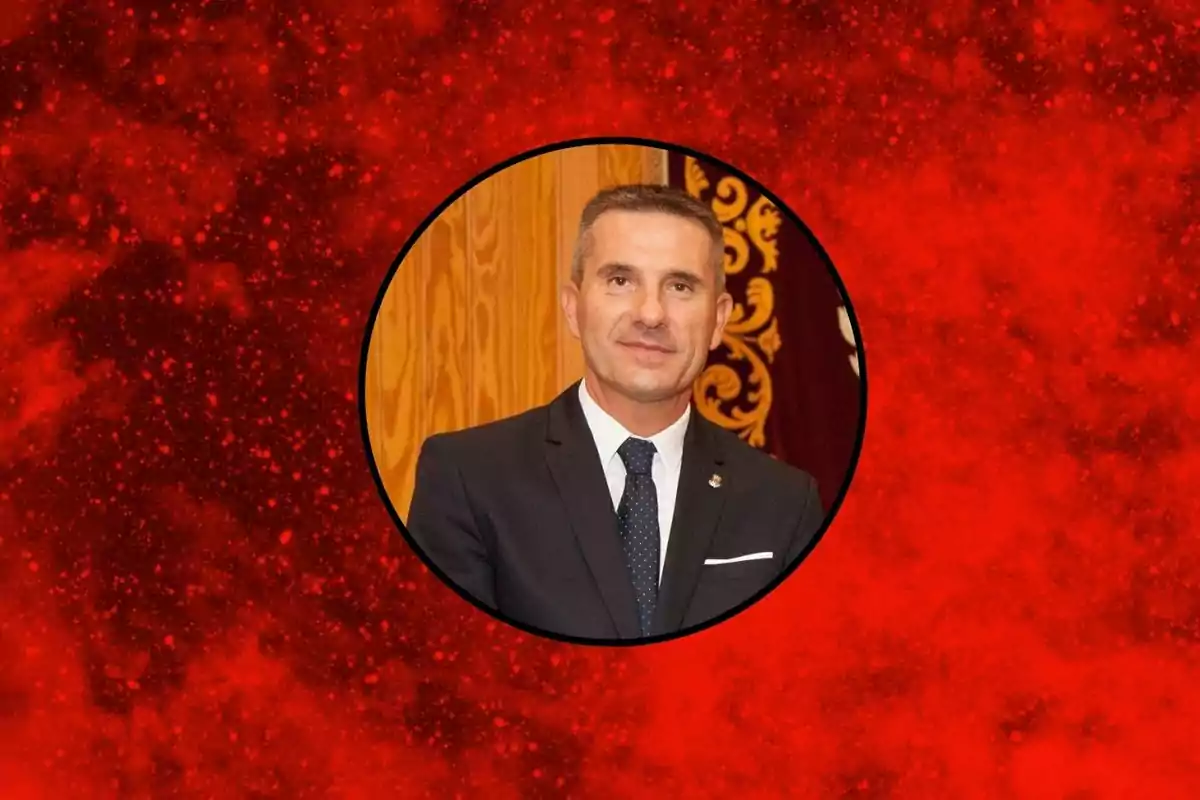 Hombre de traje oscuro y corbata posando frente a un fondo de madera dentro de un círculo sobre un fondo rojo texturizado