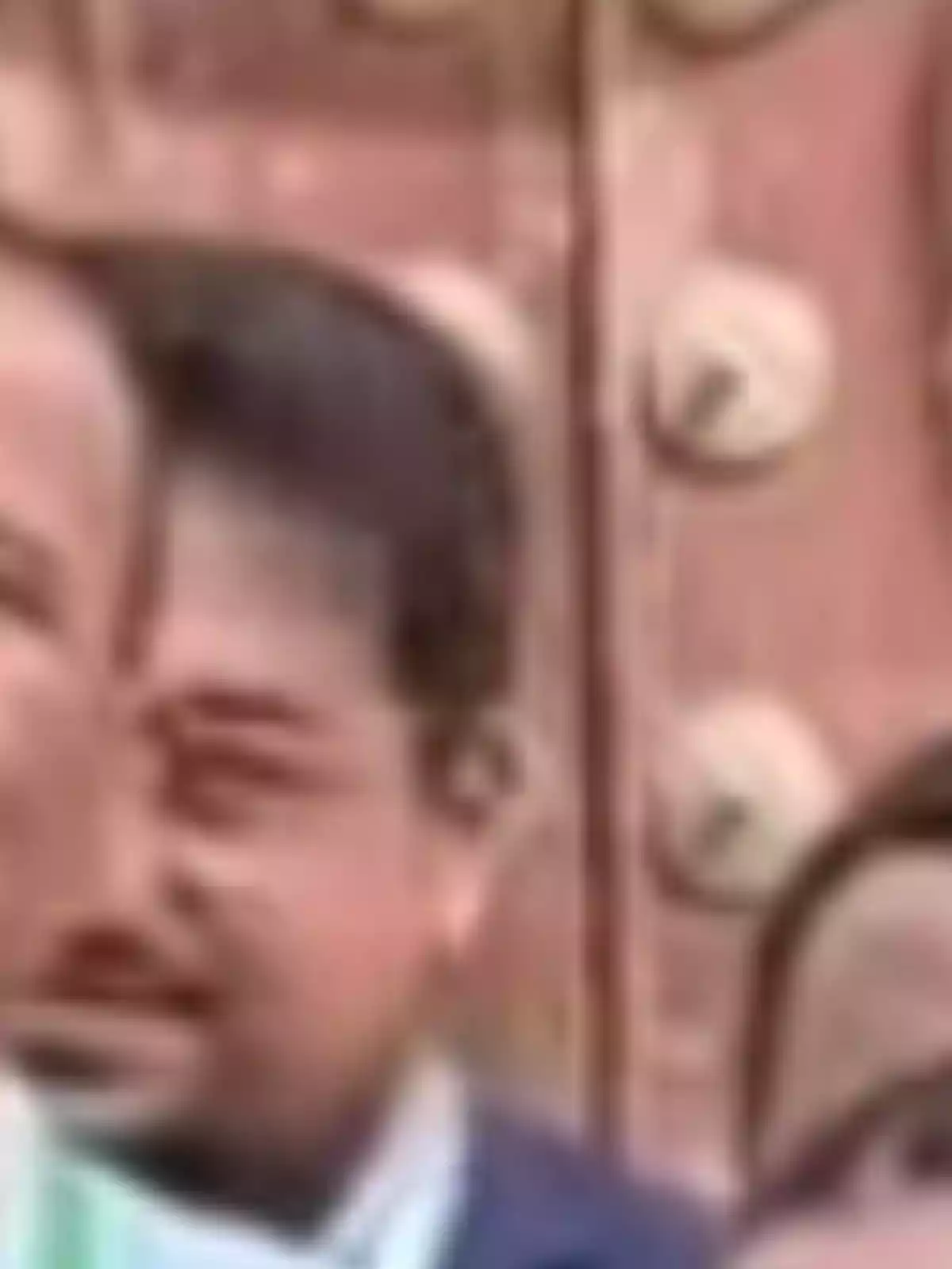 Hombre de cabello oscuro con barba corta y traje, imagen borrosa y fondo marrón con detalles circulares Hombre de cabello oscuro con barba corta y traje, imagen borrosa y fondo marrón con detalles circulares