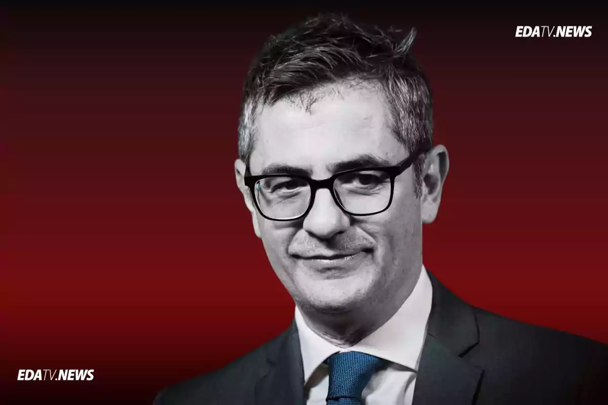 Hombre de cabello corto y canoso con gafas y traje oscuro sobre fondo rojo con logotipos de EDATV NEWS en las esquinas