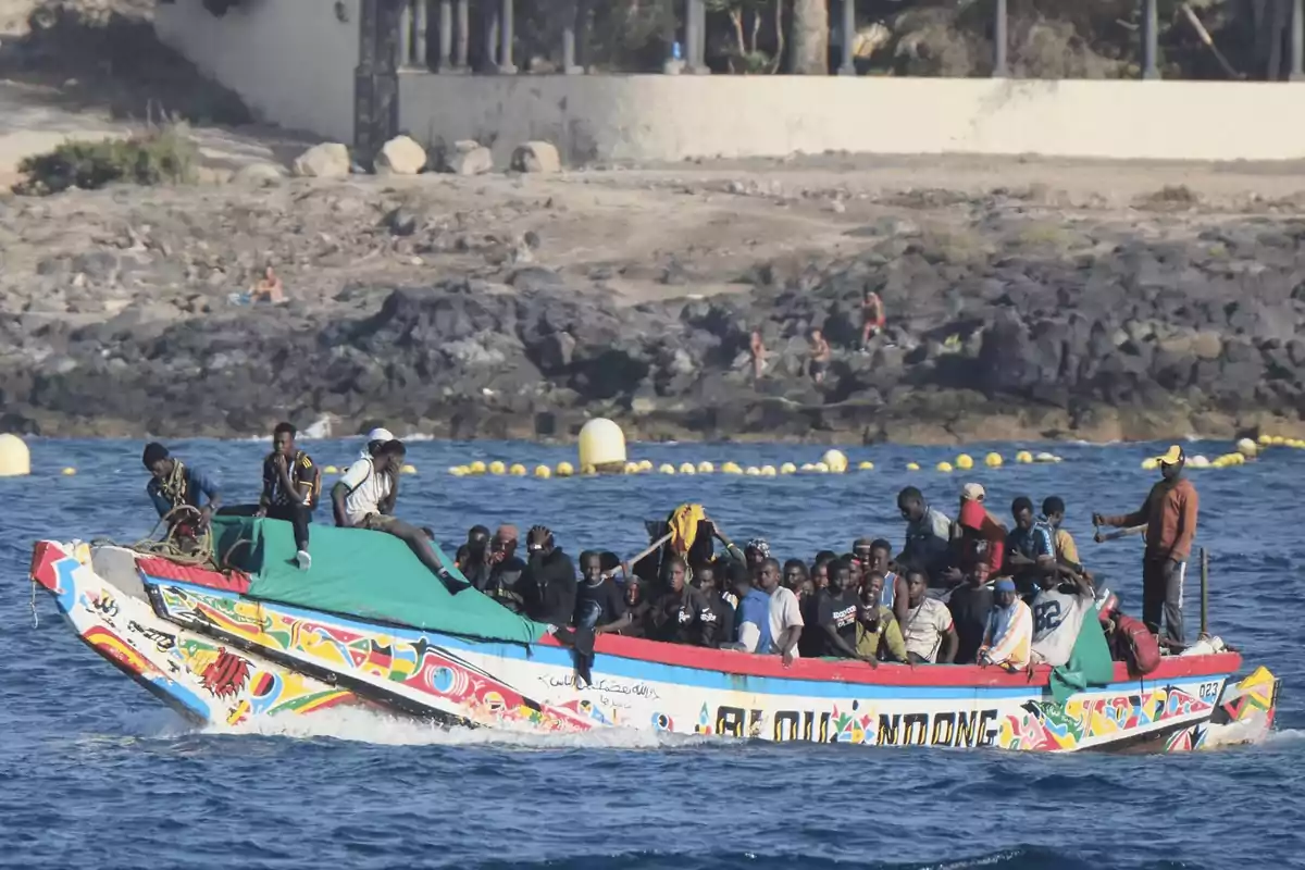Un grupo numeroso de personas viaja en una embarcación colorida sobre el mar, cerca de una costa rocosa. Un grupo numeroso de personas viaja en una embarcación colorida sobre el mar, cerca de una costa rocosa.