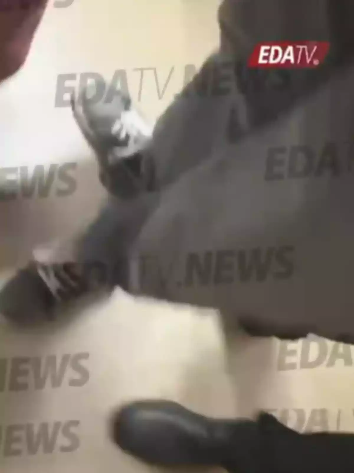 Varias personas de pie en el suelo, algunas usando zapatos oscuros y otras zapatillas deportivas, con la marca de agua EDA TV NEWS sobre la imagen.