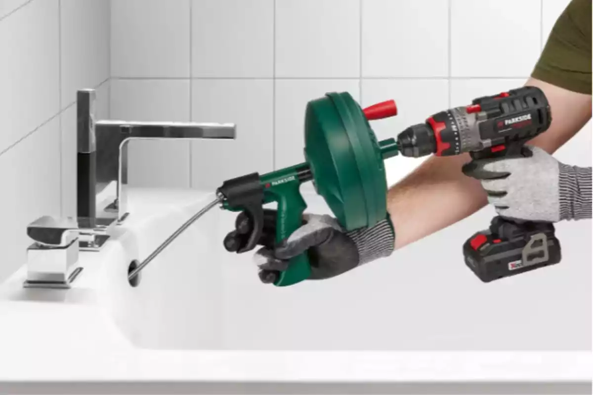 Persona usando un taladro y una herramienta de fontanería para destapar el desagüe de un lavabo blanco en un baño. Persona usando un taladro y una herramienta de fontanería para destapar el desagüe de un lavabo blanco en un baño.