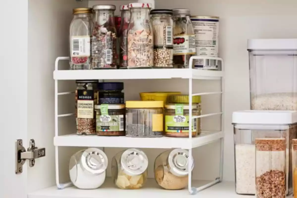 Estante organizador de cocina con frascos de especias y recipientes de alimentos almacenados ordenadamente dentro de un gabinete blanco