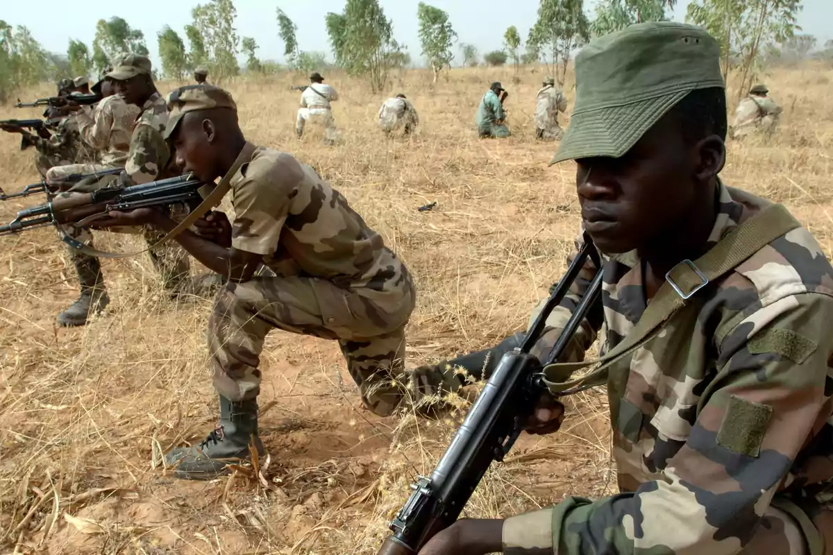 Soldados con uniforme de camuflaje realizan ejercicios de entrenamiento militar en un campo seco y abierto Soldados con uniforme de camuflaje realizan ejercicios de entrenamiento militar en un campo seco y abierto