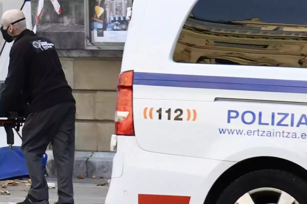 Un hombre con mascarilla empuja una camilla junto a una furgoneta de la policía con el número de emergencia 112 y la palabra Polizia escrita en el lateral