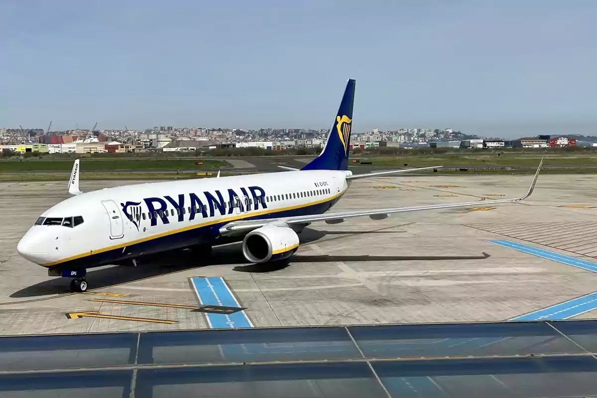 Avión de la aerolínea Ryanair estacionado en la pista de un aeropuerto con la ciudad al fondo Avión de la aerolínea Ryanair estacionado en la pista de un aeropuerto con la ciudad al fondo