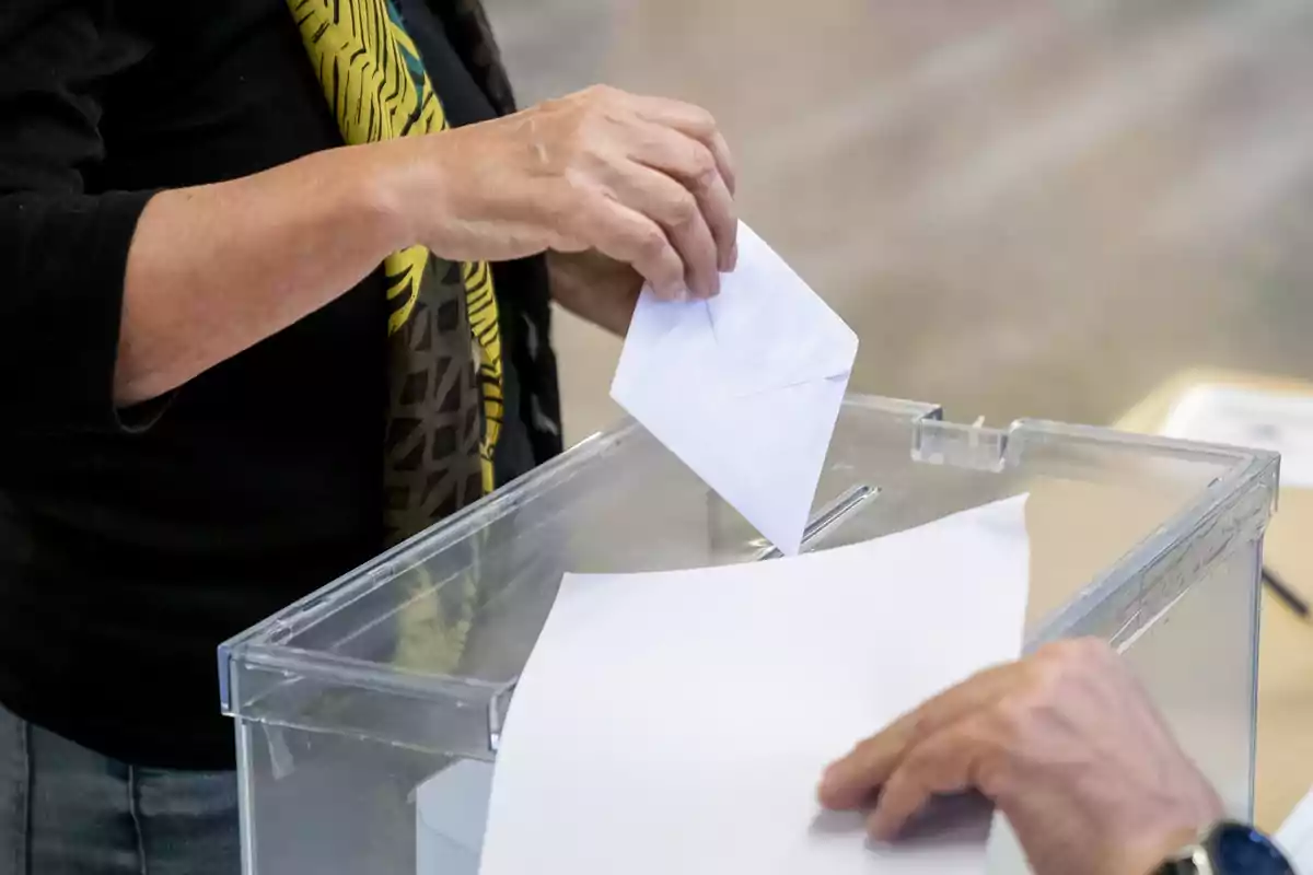 Persona depositando un sobre en una urna transparente durante una votación Persona depositando un sobre en una urna transparente durante una votación