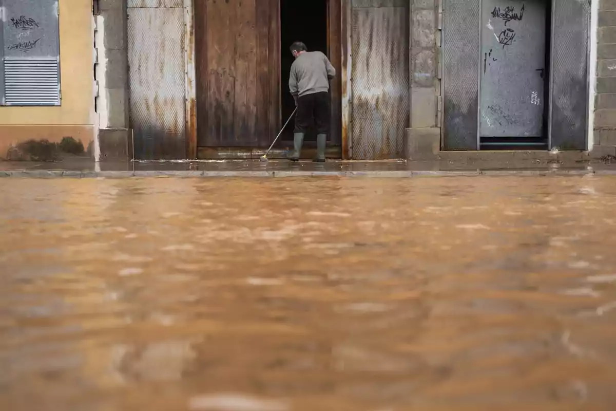 Persona con botas limpiando la entrada de una casa durante una inundación Persona con botas limpiando la entrada de una casa durante una inundación
