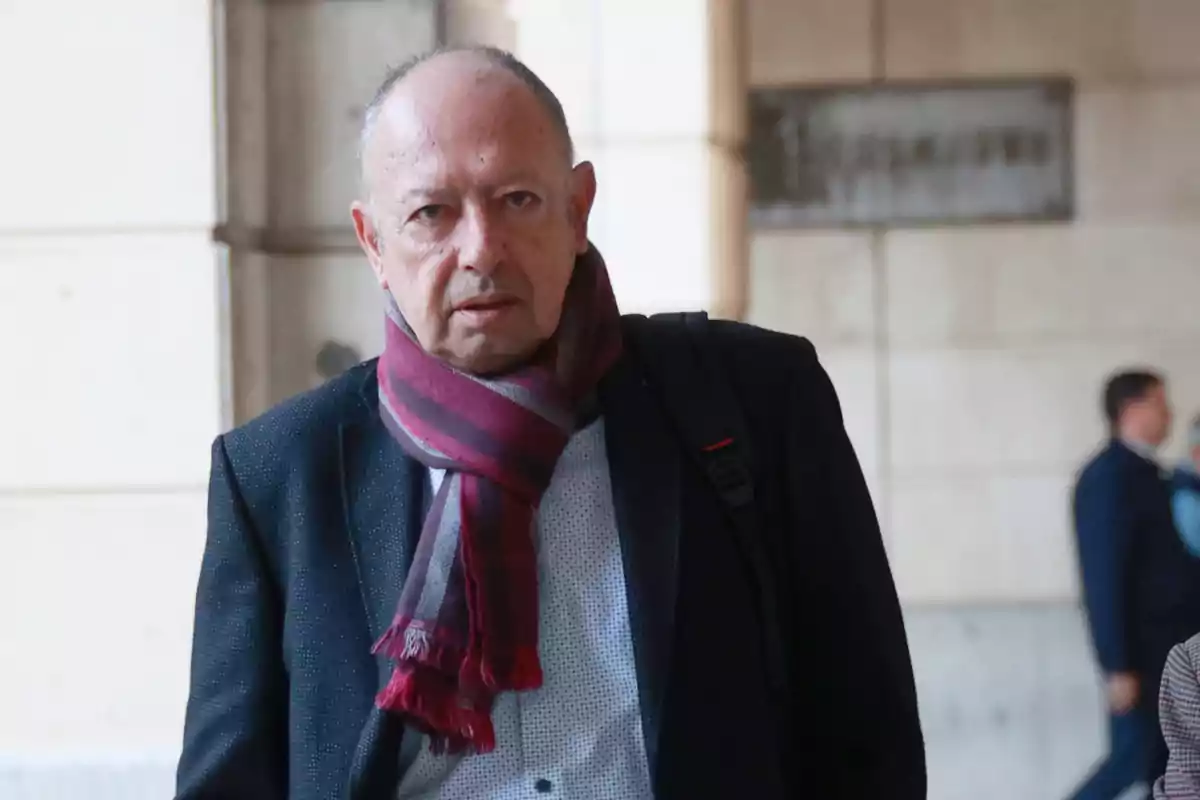 Hombre de mediana edad con bufanda roja y chaqueta oscura caminando en un entorno urbano Hombre de mediana edad con bufanda roja y chaqueta oscura caminando en un entorno urbano